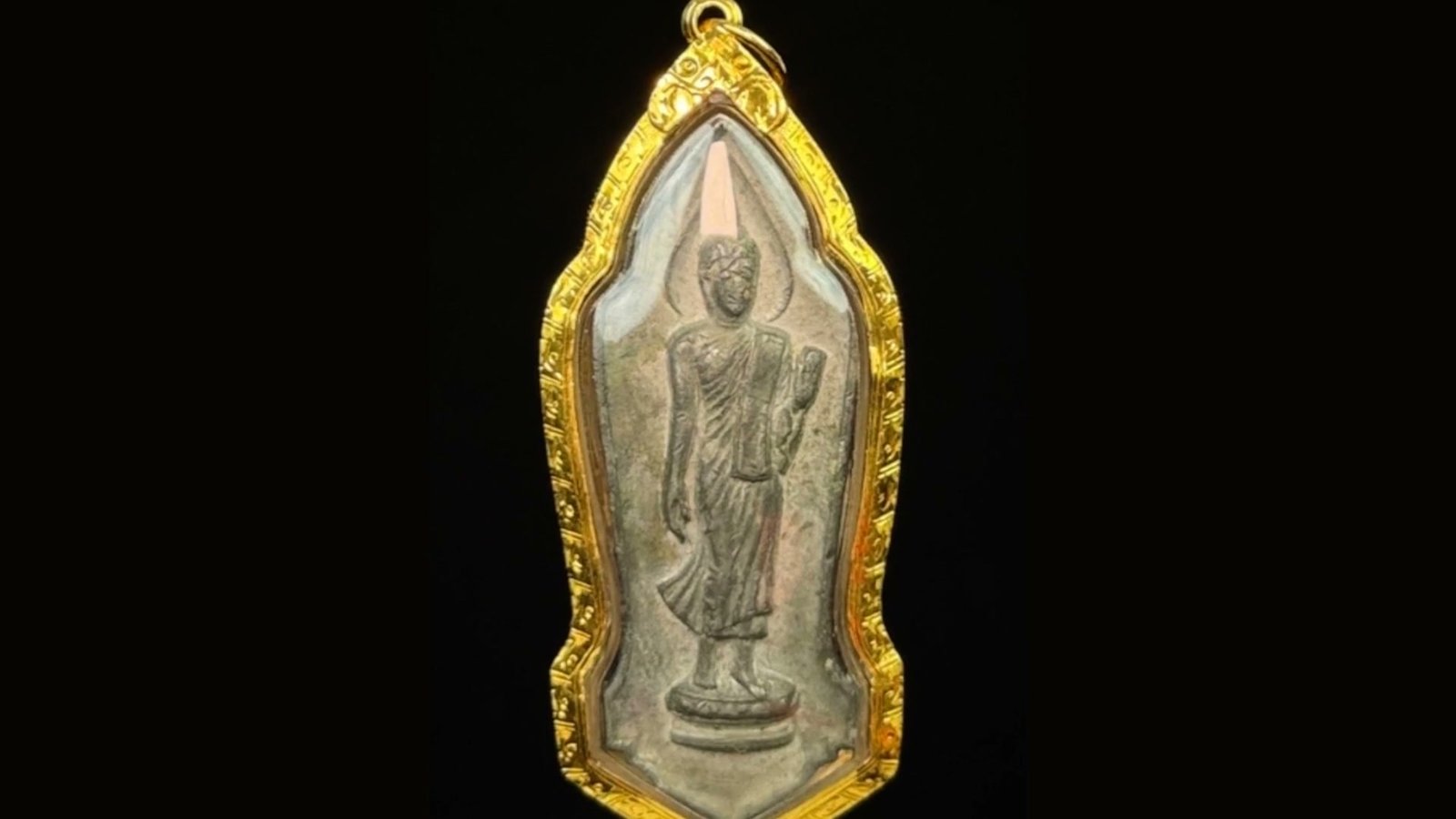 Walking Buddha amulet in an engraved gold case, resting on the bench